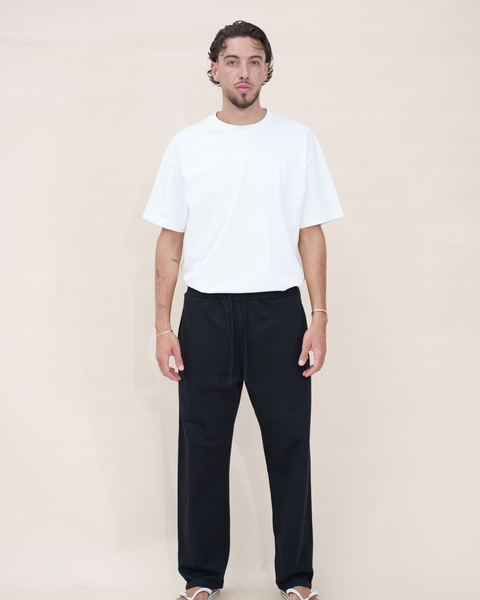 The Cotton Tee — t-shirt oversize en coton homme The Fit Society, blanc, porté avec un pantalon large noir, de face