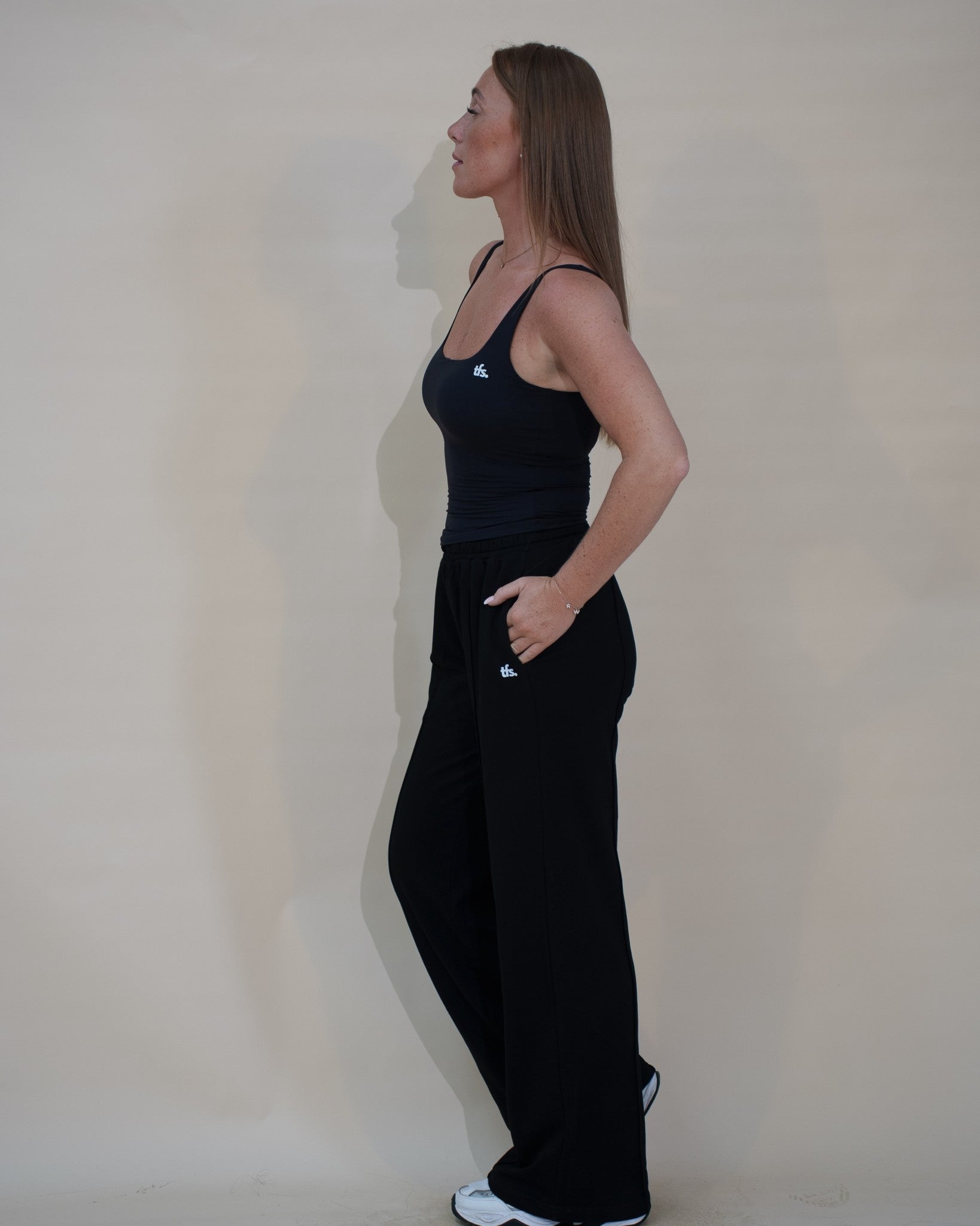 The Uniform Pants — pantalon large femme The Fit Society, noir, de profil, porté avec The Uniform Top