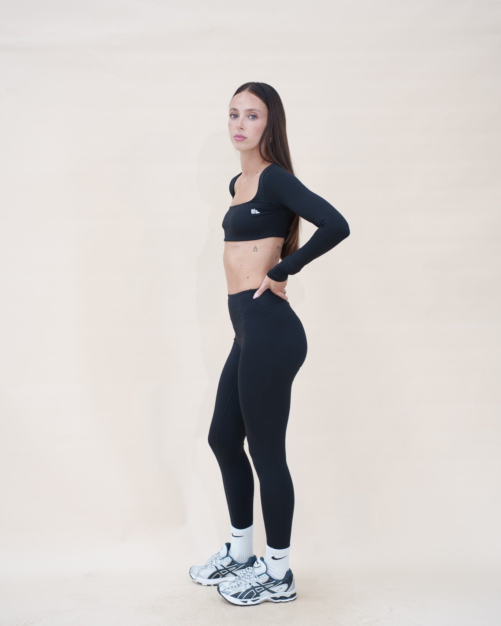 Le vestiaire Studio The Fit Society — haut noir porté avec The Studio Legging, de profil